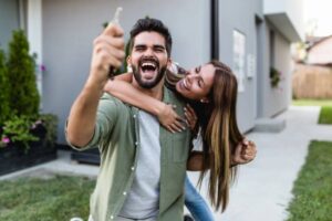 uomo che esulta con in mano una chiave di casa e donna che lo abbraccia da dietro