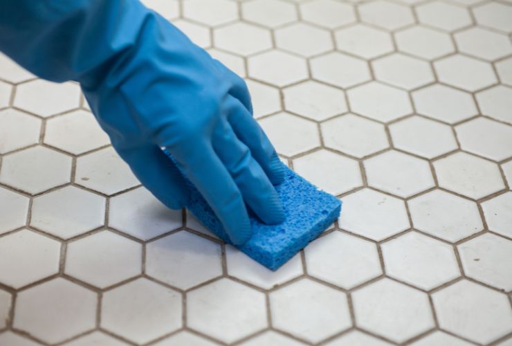 donna che pulisce fughe del pavimento con guanti e spugna 